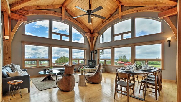 A spacious living area with a high ceiling, large windows, a fireplace, and a dining area. - Home w/ Kachemak Bay View - 5 Miles to Downtown! (Homer)