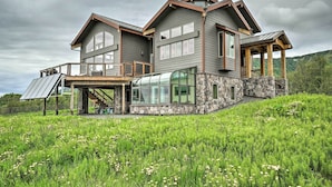 A large, modern house with a stone foundation, large windows, and a covered outdoor area. - Home w/ Kachemak Bay View - 5 Miles to Downtown! (Homer)