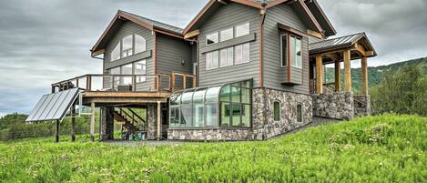 A large, modern house with a stone foundation, large windows, and a covered outdoor area.