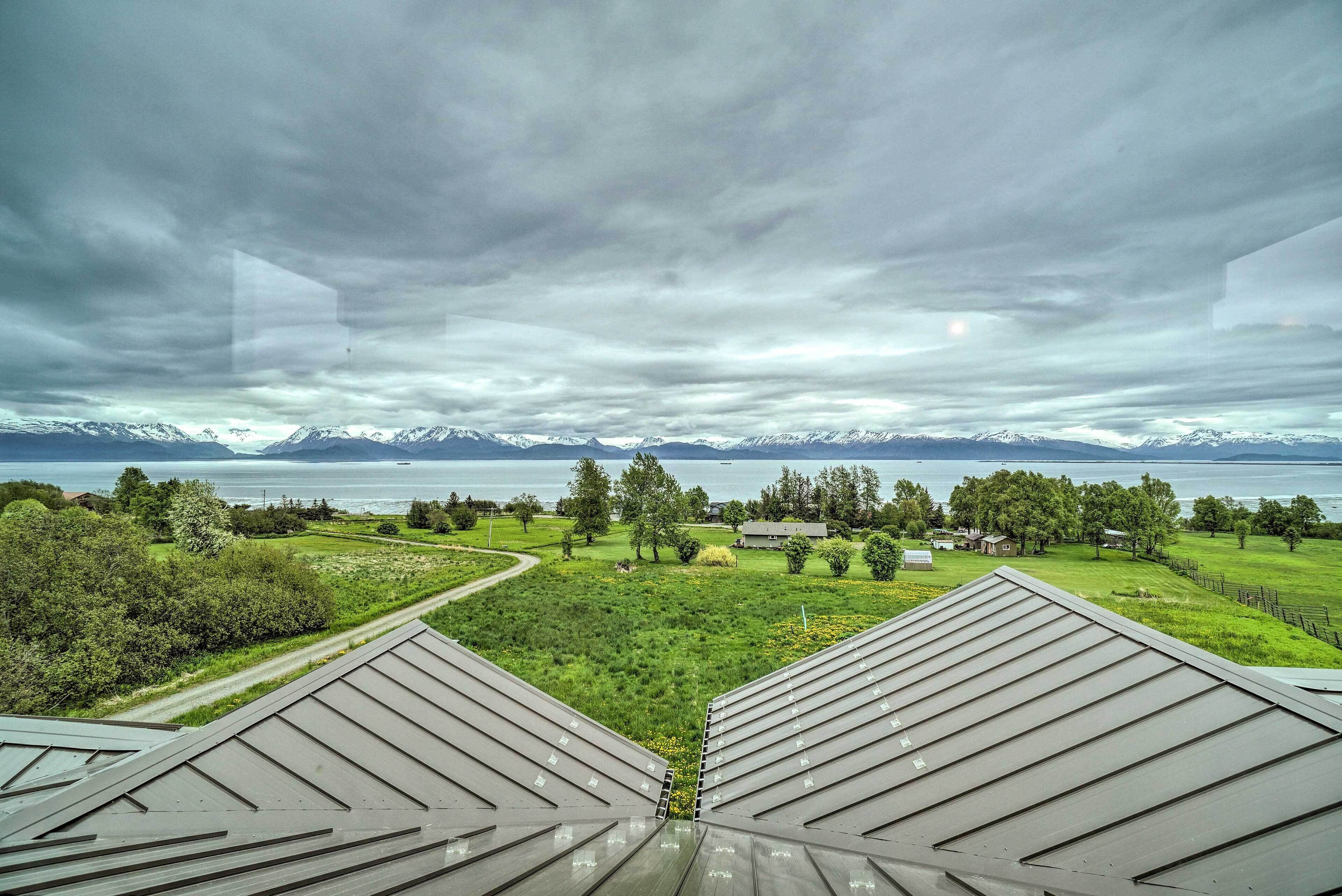 A view from a building's roof overlooking a green landscape with a lake and mountains in the distance.