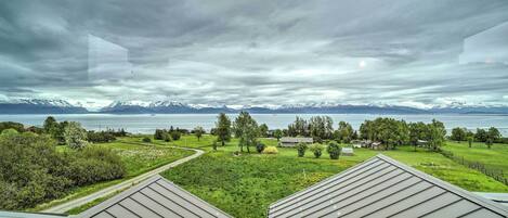 A view from a building's roof overlooking a green landscape with a lake and mountains in the distance.