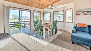 Une pièce avec un plafond en bois, une table à manger avec des chaises, un canapé bleu et de grandes fenêtres équipées de stores.