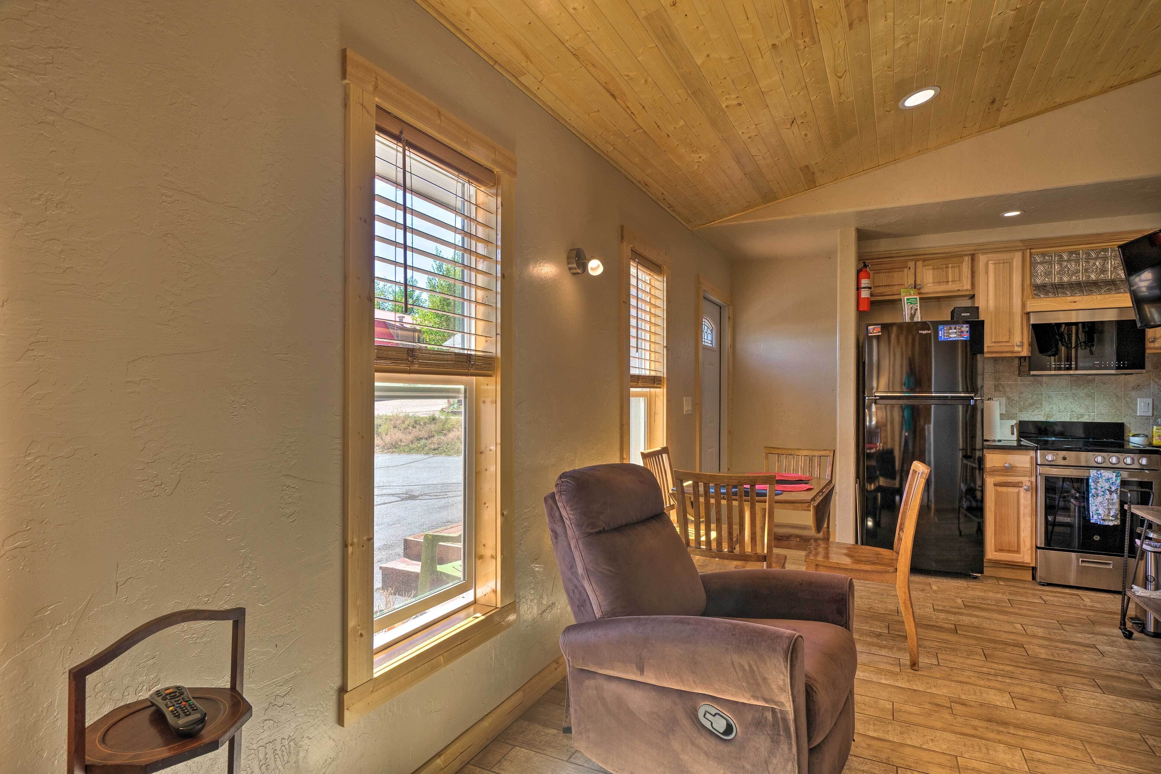 A cozy interior with a wooden ceiling, a kitchen area with modern appliances, and a seating area with a recliner and a wooden chair.
