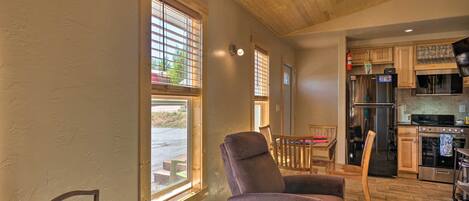A cozy interior with a wooden ceiling, a kitchen area with modern appliances, and a seating area with a recliner and a wooden chair.