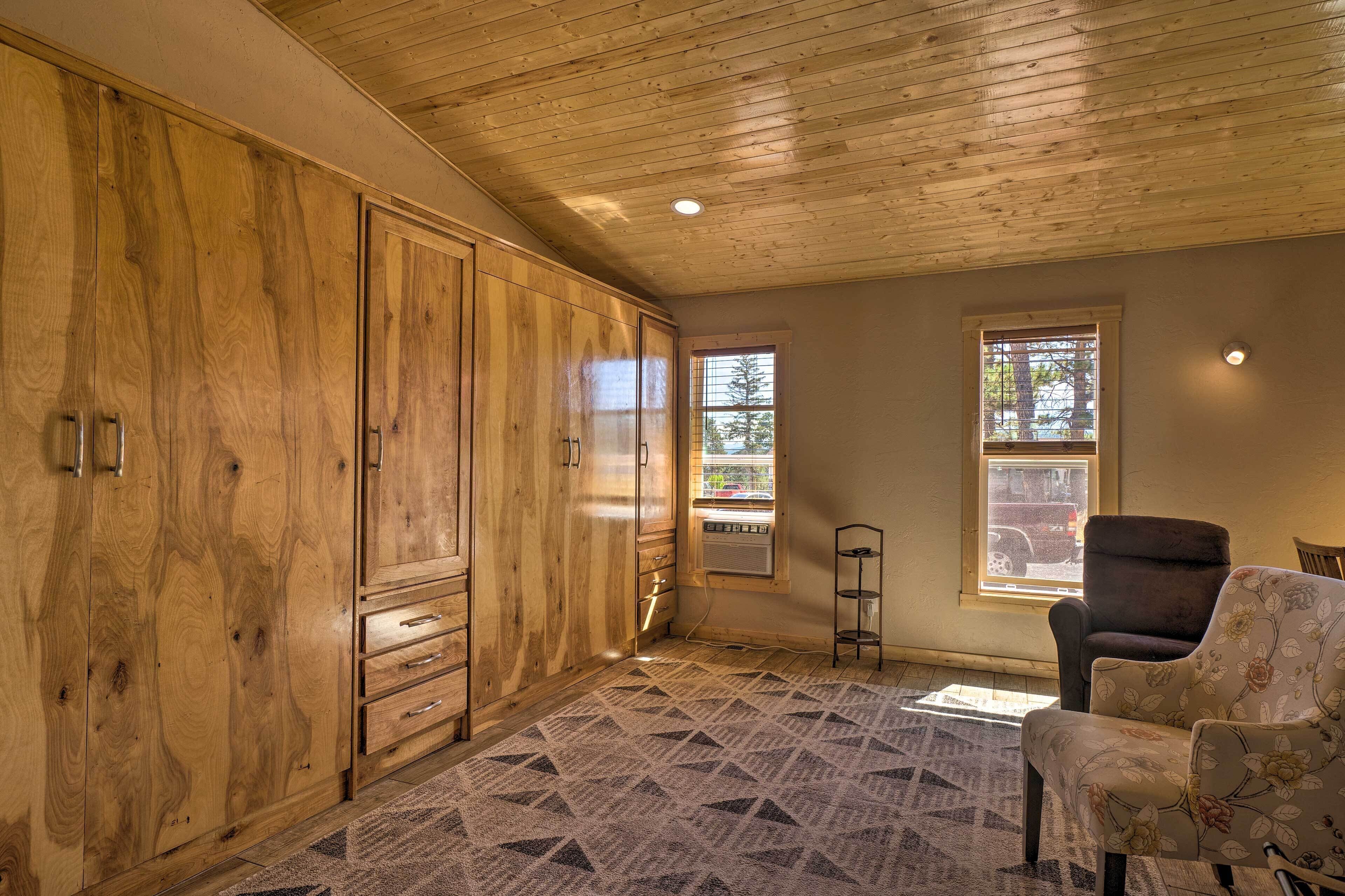 Une pièce avec des meubles de rangement en bois, un tapis à motifs, une chaise et deux fenêtres équipées de stores.