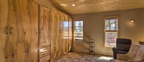A room with wooden cabinets, a patterned rug, a chair, and two windows with blinds.