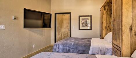 A bedroom with two beds, a wooden wardrobe, a flat-screen TV, and a framed picture on the wall.