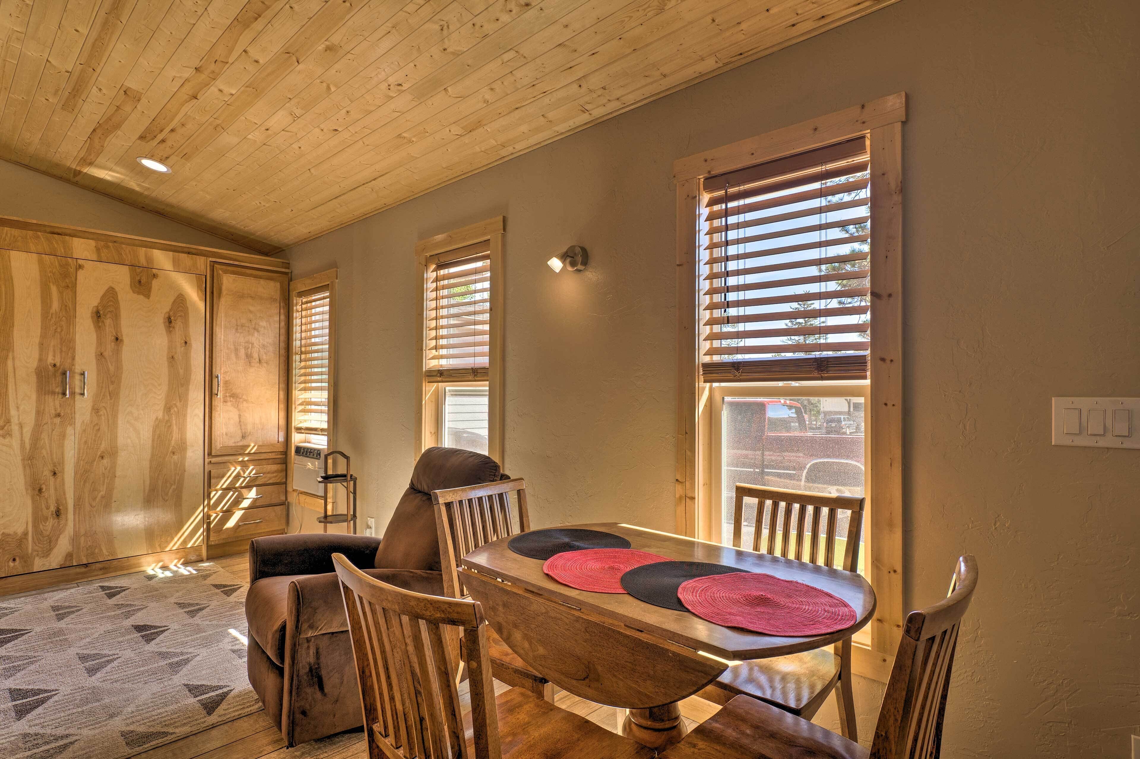 A dining area with a wooden table, chairs, and a view through large windows.