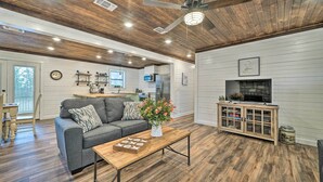 A modern living room with a wooden ceiling, a grey sofa, a coffee table with a vase of flowers, and a TV cabinet. - Updated Family Home, 20 Mi to Broken Bow Lake! (Bethel)