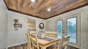 A dining area with a wooden table and chairs, a sign indicating a laundry service, and a view through a door. - Updated Family Home, 20 Mi to Broken Bow Lake! (Bethel)