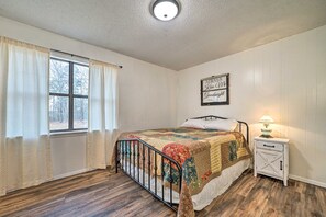 Un dormitorio con cama, una mesita de noche, una lámpara, una ventana con cortinas y una pared con un cartel.