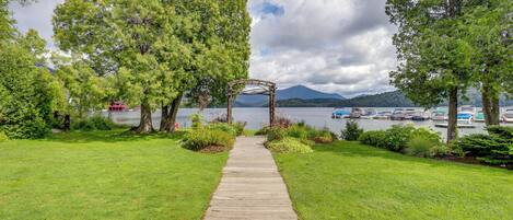 A wooden pathway leading to a gazebo by a lake with boats and mountains in the background.