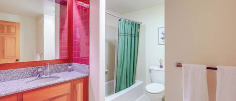 A bathroom with a wooden vanity, a sink, a mirror, a bathtub, and a toilet.