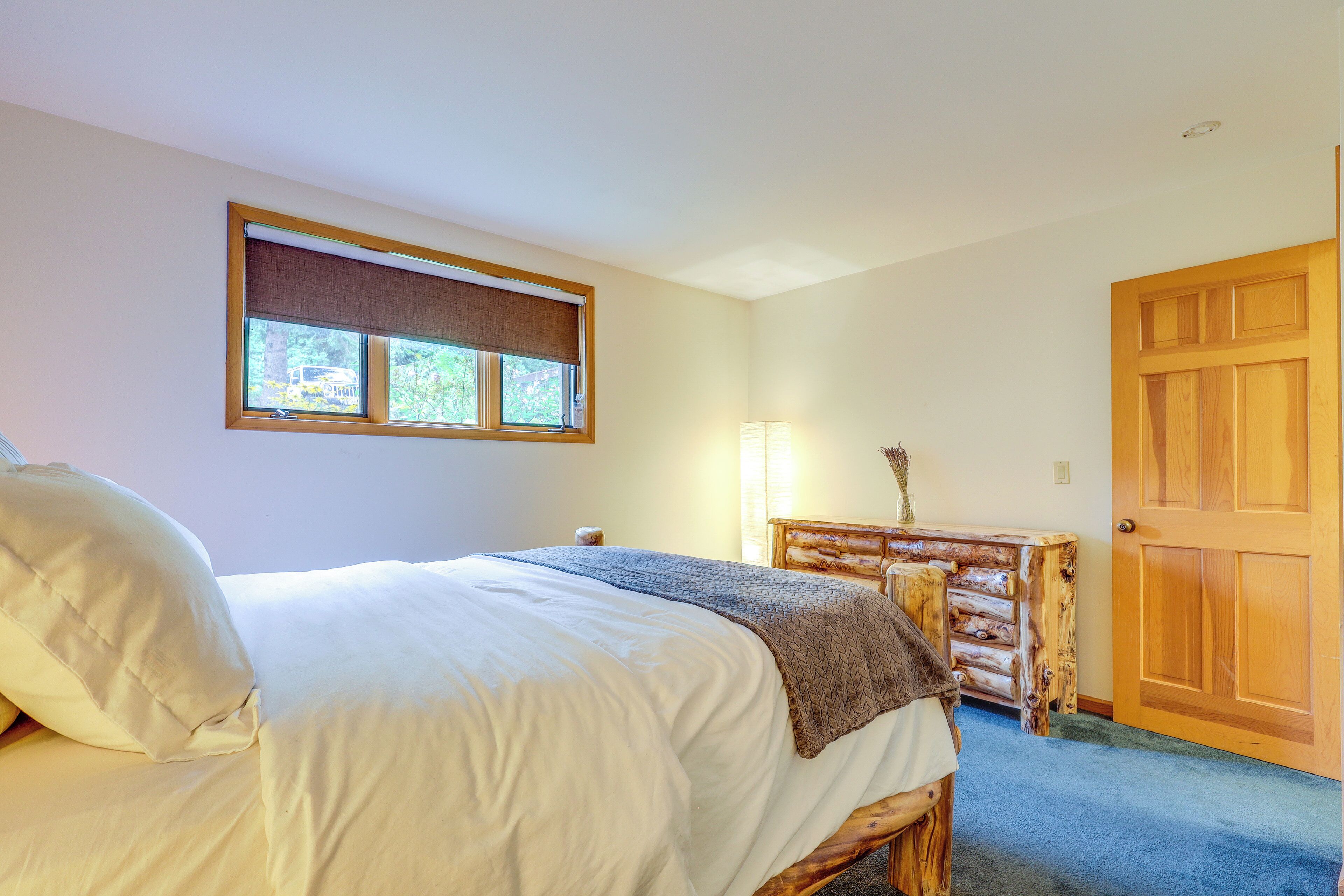 Un dormitorio con una cama, un aparador de madera, una lámpara y una puerta.