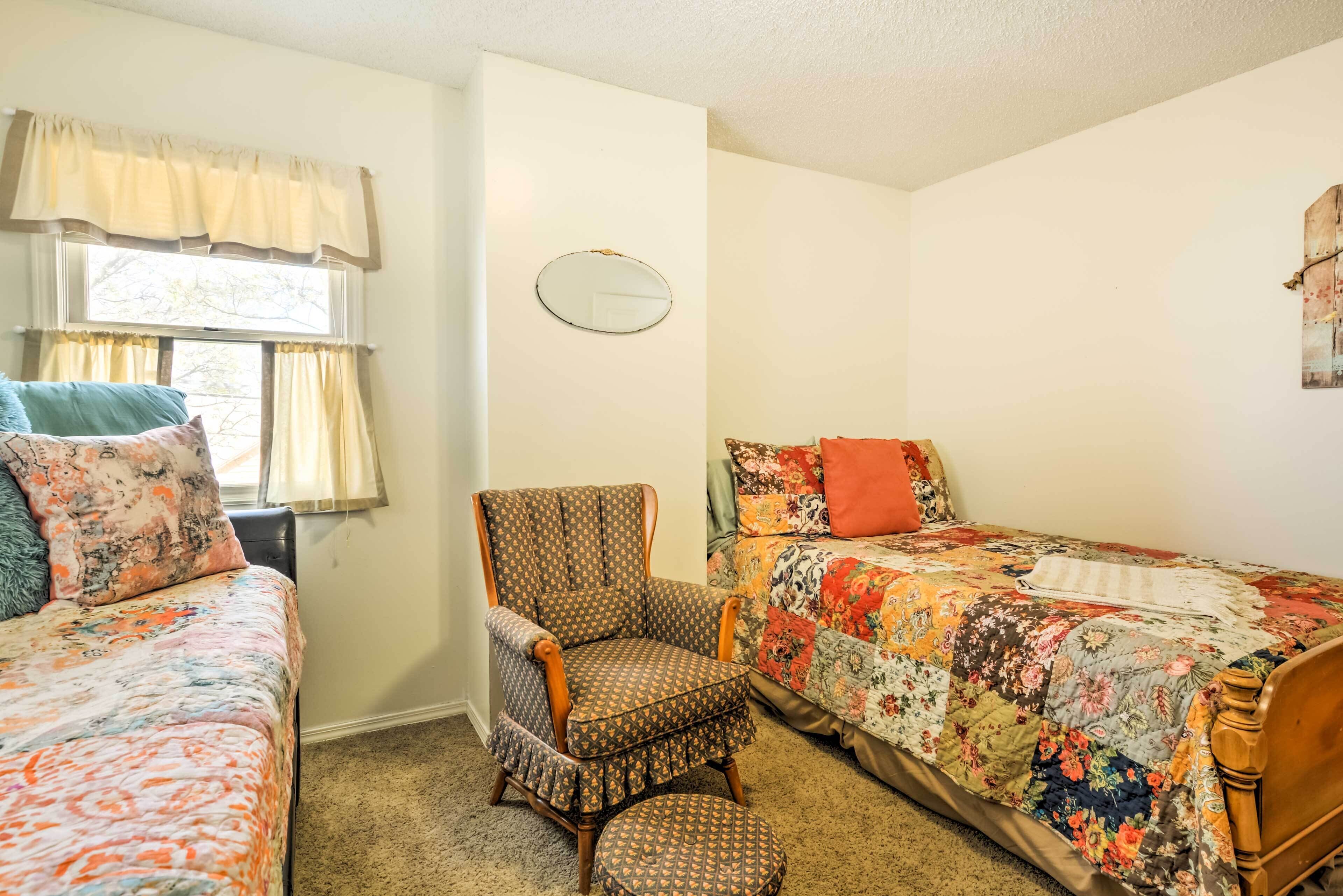 A bedroom with two beds, a chair, and a mirror.