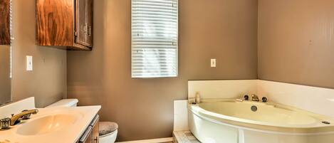 A bathroom with a bathtub, toilet, sink, vanity, and a window with blinds.