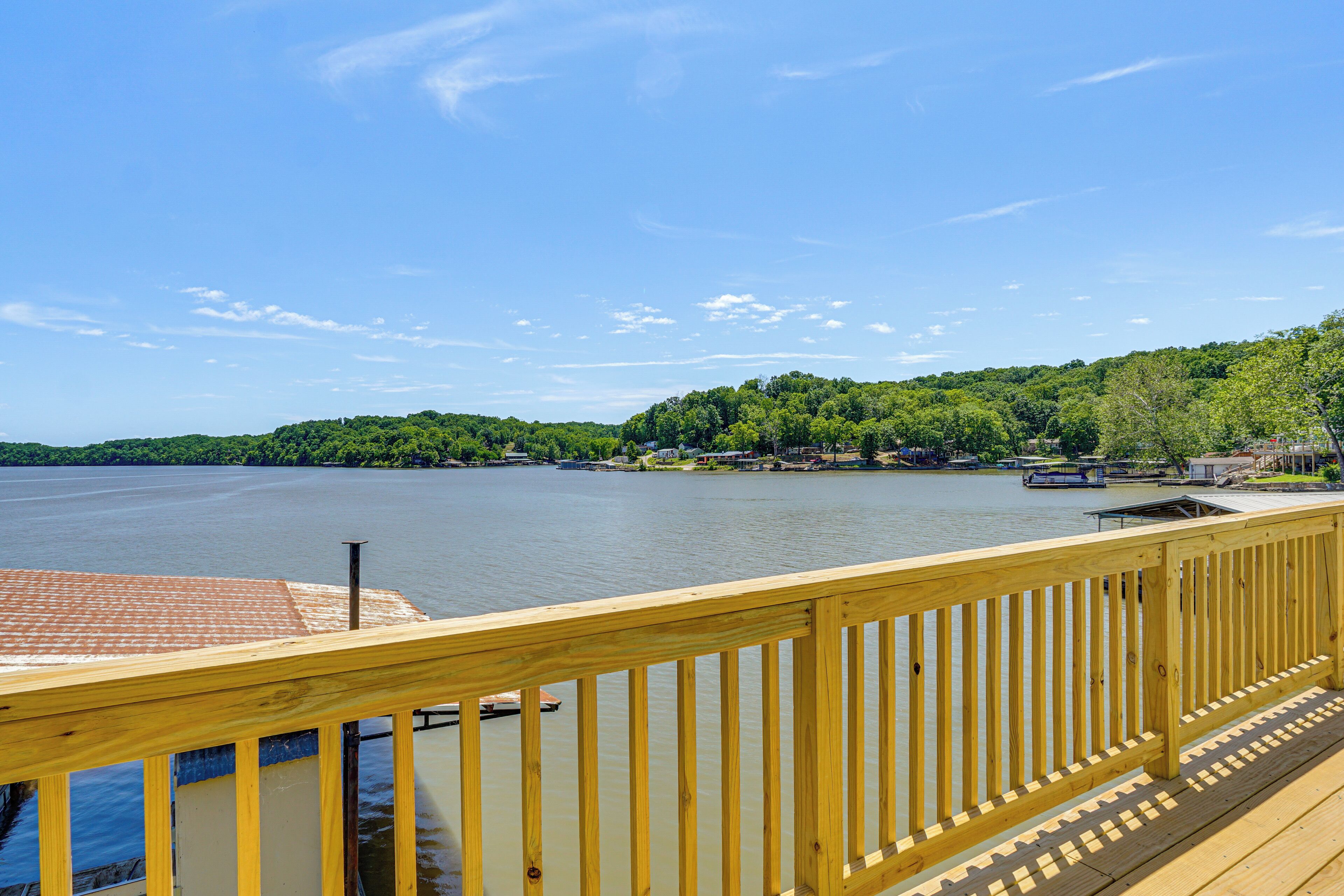 A wooden deck overlooking a calm lake with a forested hill in the background.