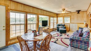 A wooden-paneled room with a dining table, chairs, a sofa, and a television. - Deck w/ Covered Dock! Lakefront Ozark Cottage (Climax Springs)