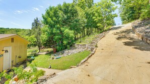 A yellow building with a door and windows, surrounded by greenery and a paved path. - Deck w/ Covered Dock! Lakefront Ozark Cottage (Climax Springs)