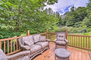 A wooden deck with wicker furniture, including a sofa and armchair, surrounded by lush greenery and trees. - Furnished Deck + Home Gym: Bakersville Retreat! (Bakersville)