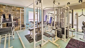 A gym with various exercise equipment, stone walls, and a window with blinds.