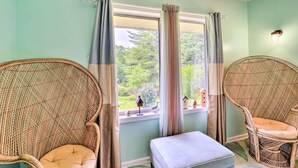 A room with two wicker chairs, a small ottoman, and a window with curtains.