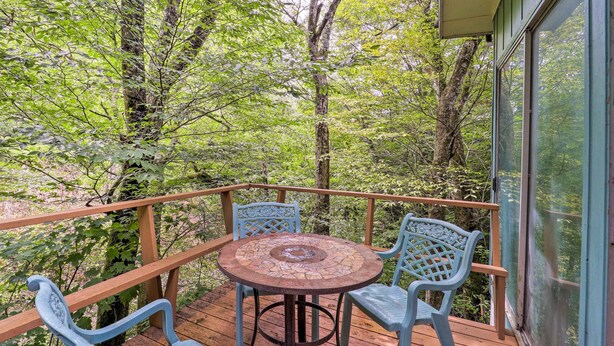 A wooden deck with a round table and two chairs, surrounded by trees.