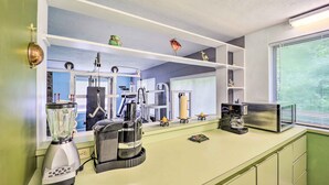 A kitchen with a blender, coffee maker, and microwave on the counter. There are shelves above the counter with decorative items.