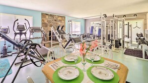 A gym with exercise equipment, a dining table set with plates and cutlery, and a stone wall.