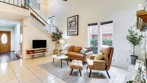 A spacious living room with a staircase, a flat-screen TV, a sofa, a coffee table, and a large window. - 4 Mi to At&t Stadium: Fort Worth Townhome! (Fort Worth)