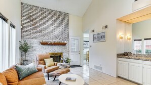 A spacious living room with a brick fireplace, a sofa, a coffee table, and a kitchen area with white cabinets and a countertop. - 4 Mi to At&t Stadium: Fort Worth Townhome! (Fort Worth)