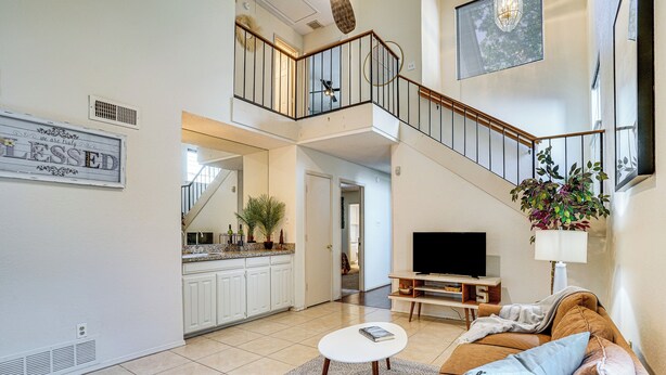 A spacious living area with a sofa, a coffee table, and a TV. A staircase connects the living area to an upper level. - 4 Mi to At&t Stadium: Fort Worth Townhome! (Fort Worth)