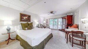 A spacious bedroom with a large bed, a desk, and a chair, a ceiling fan, and a view through a glass door to the outside. - Experience Chautauqua! Newly Renovated Studio (Mayville)