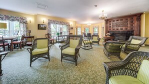 A spacious lounge with wicker furniture, a fireplace, and large windows. - Experience Chautauqua! Newly Renovated Studio (Mayville)