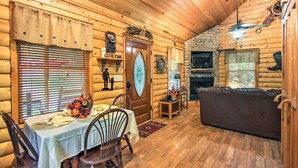 A log cabin interior with a dining area, a fireplace, and a cozy living space. - Porch & Fire Pit: Rustic Log Cabin in Smokies! (Cosby)