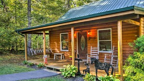 A rustic cabin with a porch, wooden benches, and a dog statue. - Porch & Fire Pit: Rustic Log Cabin in Smokies! (Cosby)