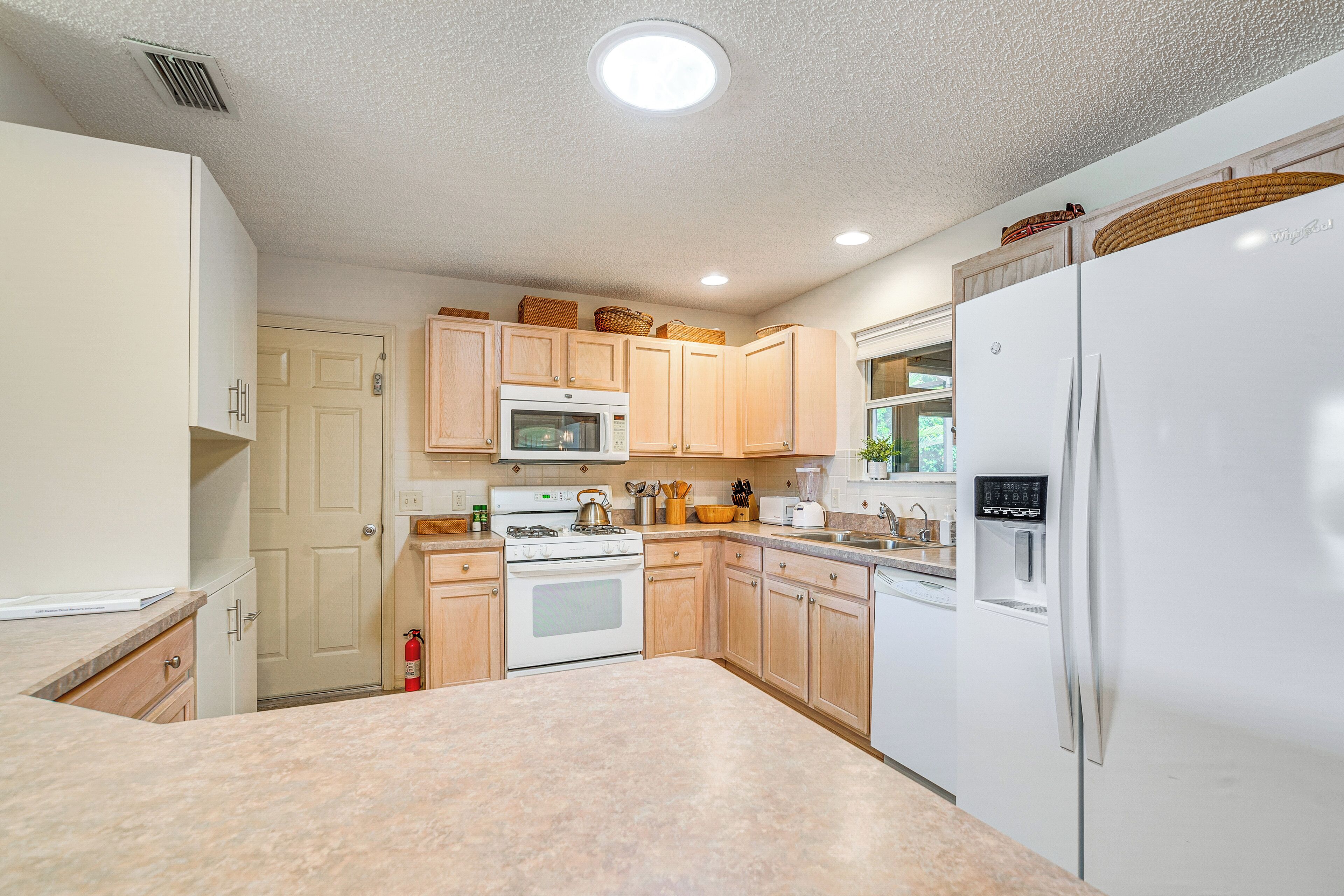 A kitchen with light wooden cabinets, a white refrigerator, a microwave, and a stove.