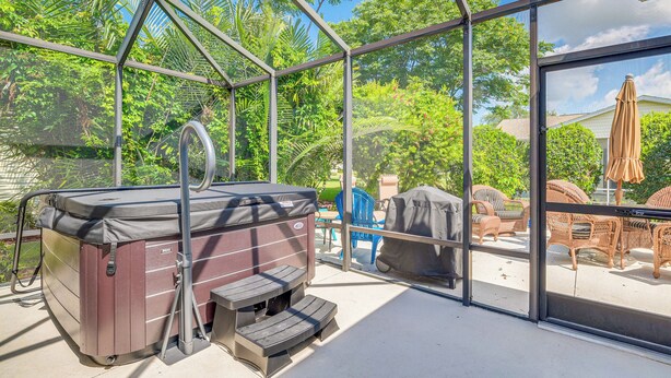 A hot tub with steps, a covered grill, and wicker furniture in a screened outdoor area. - Home in The Villages w/ Lanai & Private Hot Tub! (The Villages)