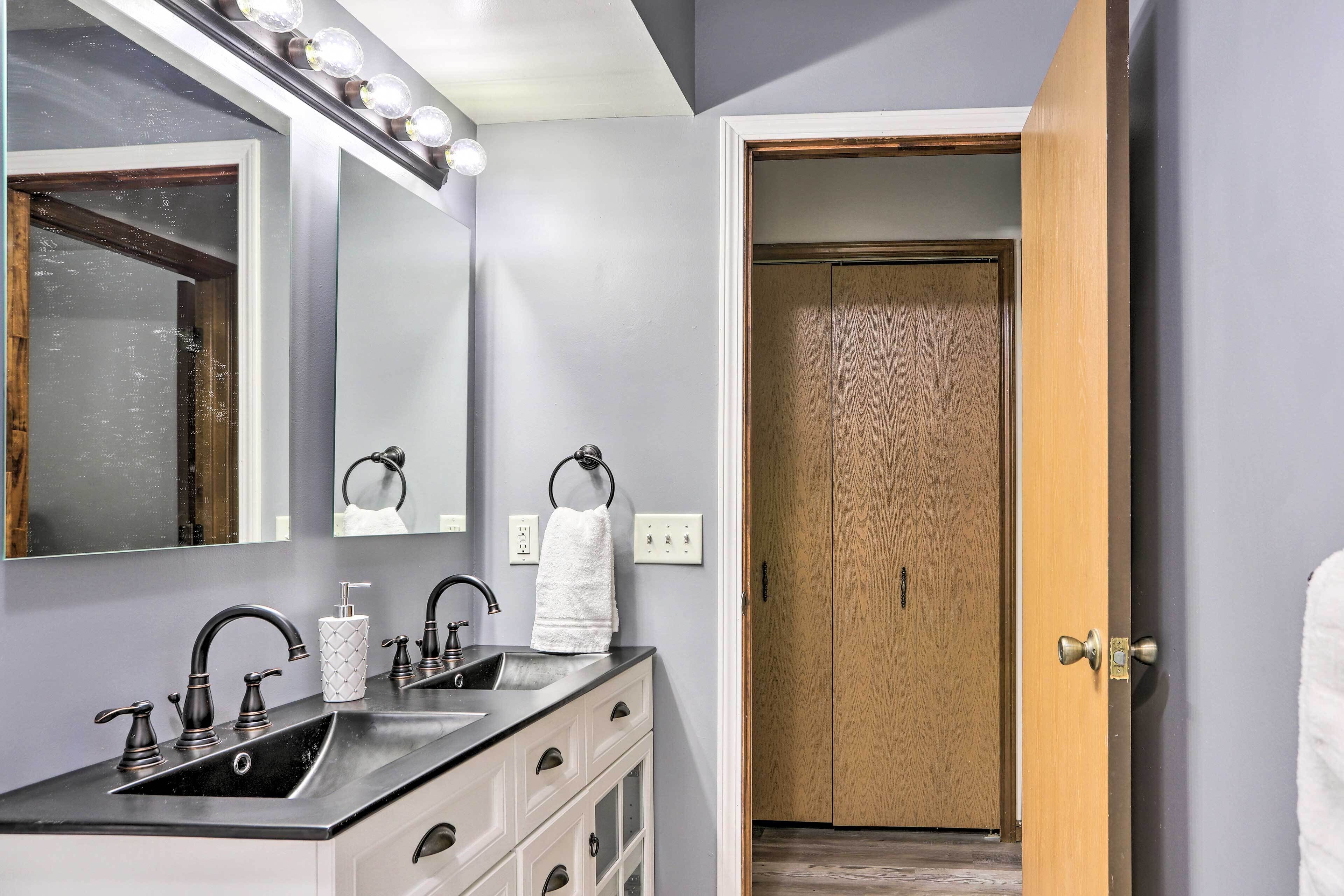 A bathroom with a vanity, a mirror with lights, a towel rack, and a wooden door.
