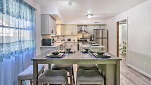 A modern kitchen with white cabinets, a stainless steel refrigerator, and a microwave. There is a dining table with four chairs and a glass top.