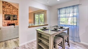 A dining area with a table set for four, a stone fireplace, and a large window with a view of greenery.