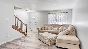 A living room with a beige sofa, patterned ottoman, and a staircase.