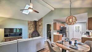 A modern kitchen with a stone accent wall, a dining area with a round table and chairs, and a living room with a sofa and a flat-screen TV. - Peaceful Cottage w/ Mtn View Near ATV Trails! (Welch)
