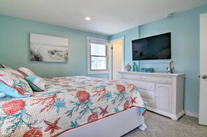 Quarto com cama, cômoda, televisão e porta.