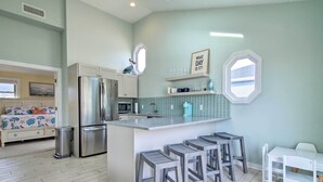 Una cucina moderna con isola centrale, sgabelli da bar e zona pranzo con tavolo e sedie bianche.