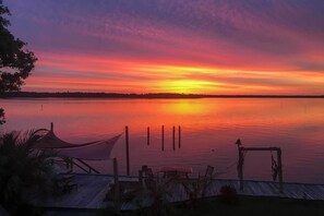 Sonnenuntergangblick von einem Steg mit Tisch, Stühlen, einem Sonnensegel und einer Schaukel.