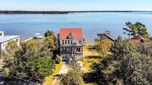 A two-story house with a red roof, surrounded by trees and a lake view. - Charming Waterfront Home: Fish, Boat + More! (Sneads Ferry)