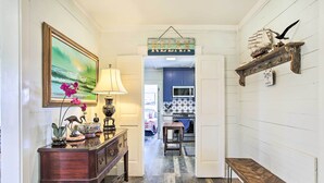 A hallway with a wooden bench, a table with a lamp, a framed painting, and a hanging sign. - Pet-friendly Surfside Beach Home w/ Deck & Grill (Freeport)
