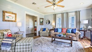 A spacious living room with a ceiling fan, a large window with curtains, and a cozy seating area with a sofa and armchairs. - Pet-friendly Surfside Beach Home w/ Deck & Grill (Freeport)