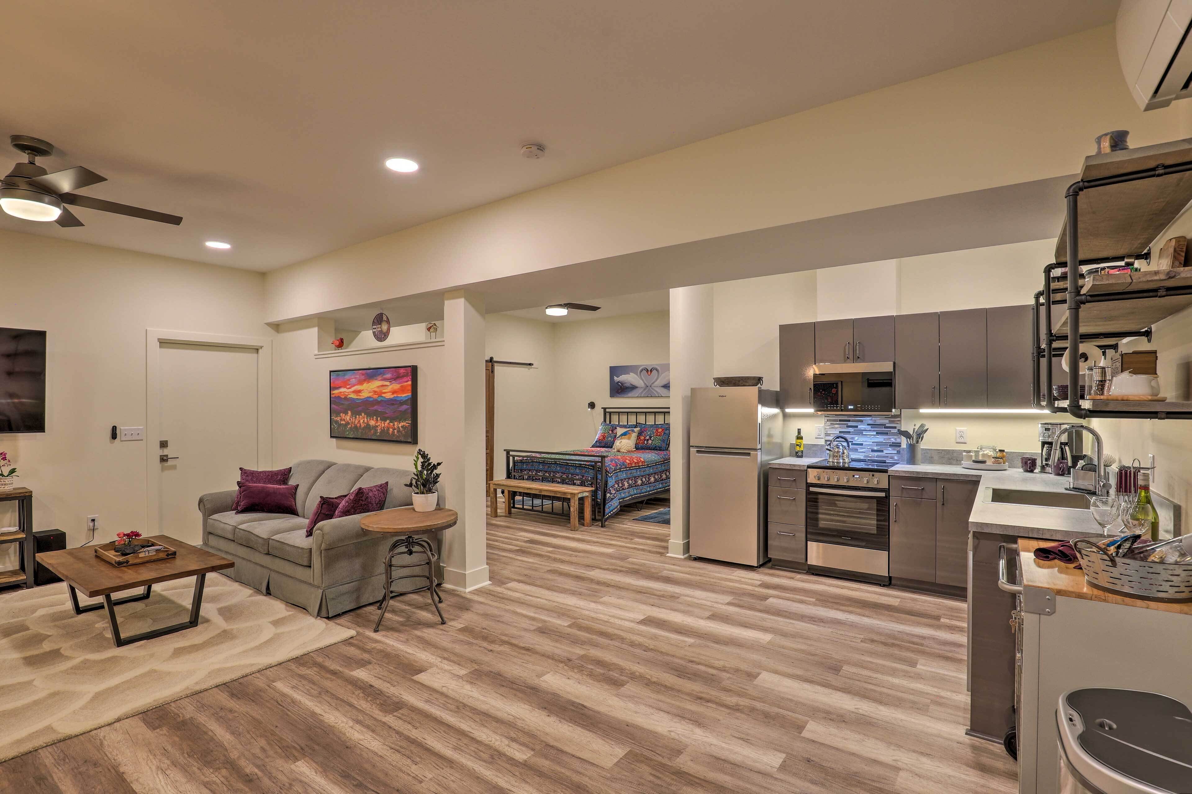 A modern living room with a sofa, coffee table, and a dining area. A kitchen with stainless steel appliances and a dining table is visible in the background.